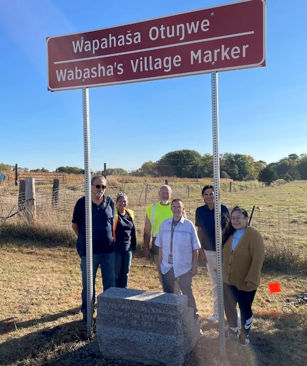 Six people standing behind granite marker. Sign above marker says Wapahasa Otunwe Wabashas Village Marker